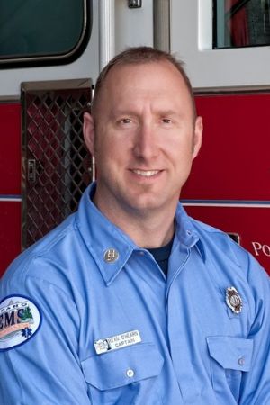 Ryan O’ Hearn (MPA, 2010), Fire Chief, City of Pocatello poses in uniform next to a red fire truck